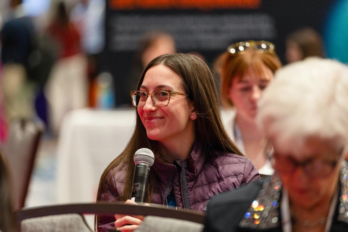 Attendee asking question into microphone in audience. 
