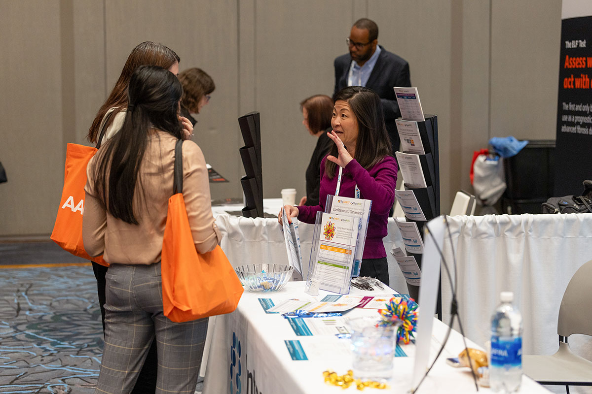 Two attendees talking with an industry partner in their exhibit booth. 