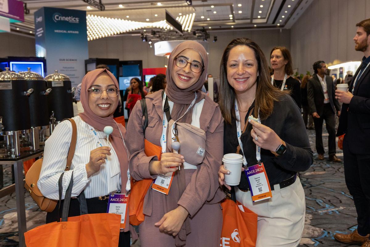 Three attendees smiling with food and drinks at a reception. 